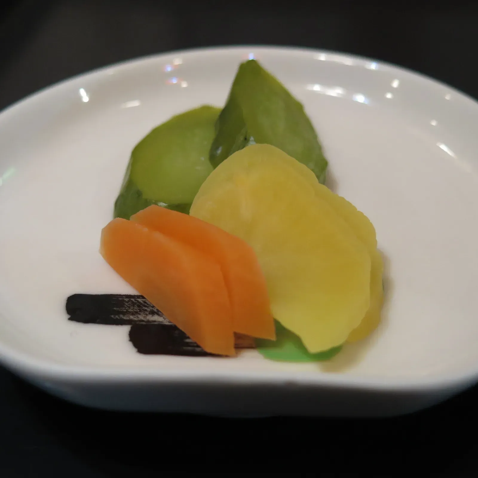 Liten vit skål med blandade tsukemono, gurka, takuan, morot och kombu